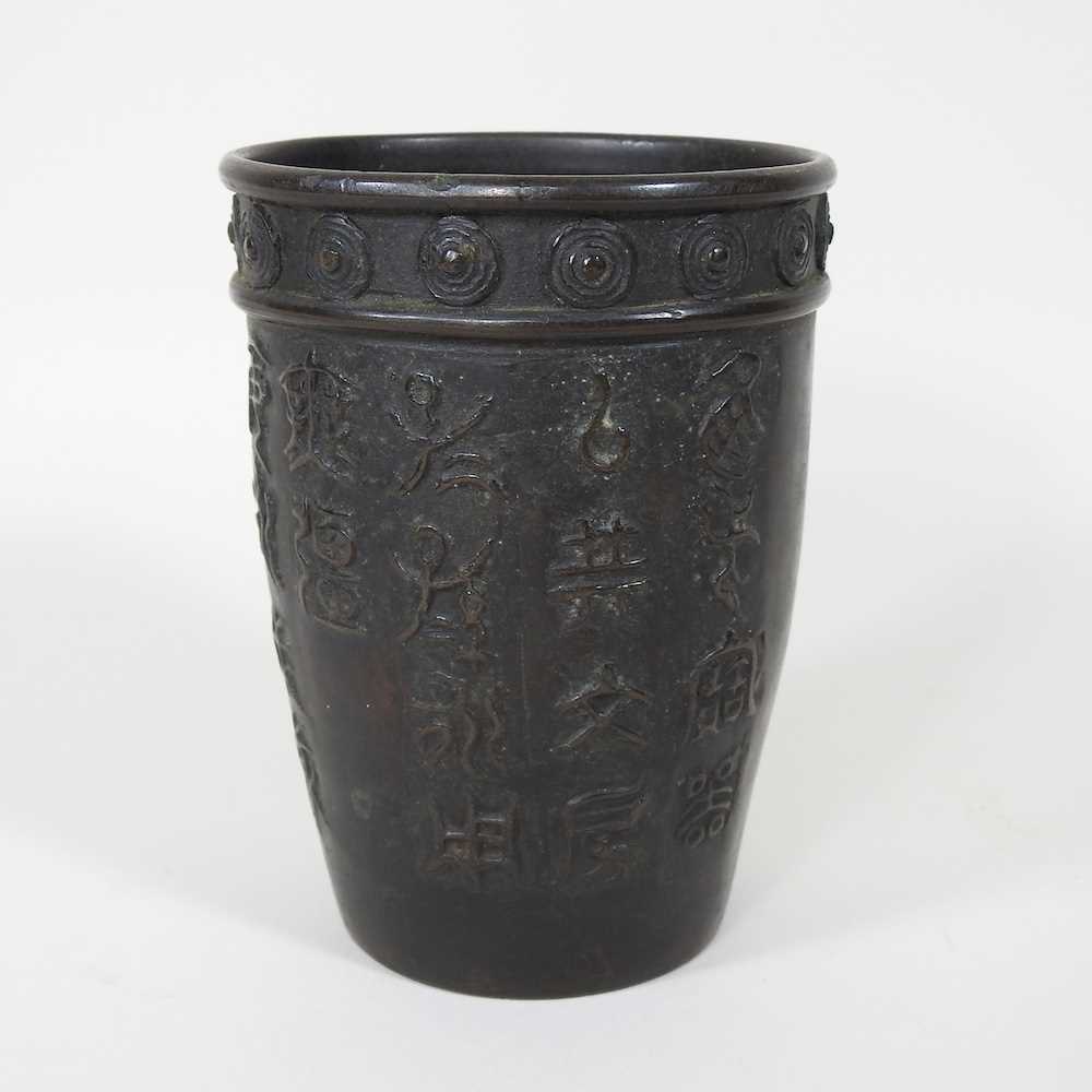 A Chinese bronze beaker, decorated in relief with symbols, signed to base, 13cm high