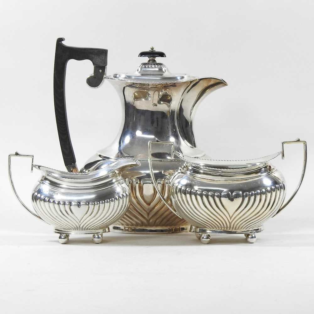 An Edwardian silver three piece tea service, with half gadrooned decoration, comprising a teapot,