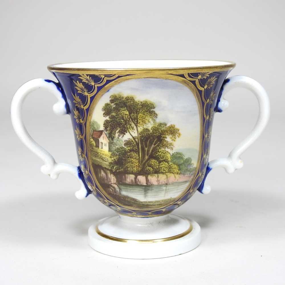 An early 19th century Derby porcelain twin handled cup, reserved with a river landscape, on a blue