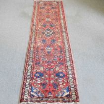 A Persian Sarouk runner, with foliate designs, on a red ground, 330 x 80cm