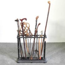 A cast iron six division stick stand, 61cm wide, containing a collection of novelty walking sticks