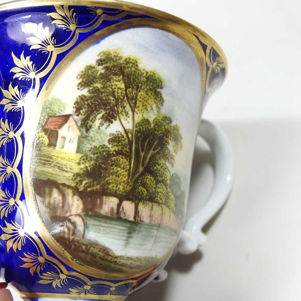 An early 19th century Derby porcelain twin handled cup, reserved with a river landscape, on a blue - Image 6 of 7