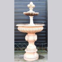 A large terracotta coloured stone garden fountain, with lion mask decoration, on a plinth base,