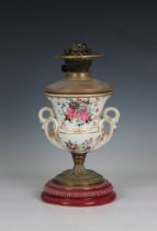 An antique ceramic urn shaped oil lamp decorated with floral sprays, twin foliate scroll handles, to