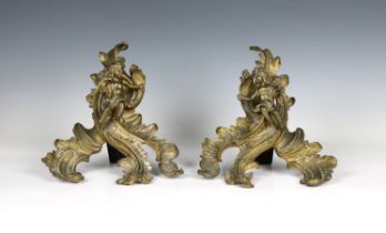 A pair of early 19th century gilt metal Rococo style chenets each featuring a cast figure of a