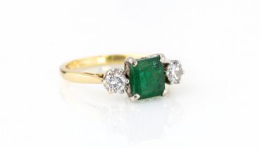 An 18ct yellow gold, emerald and diamond three stone ring the central 6.75 x 6mm. emerald flanked by