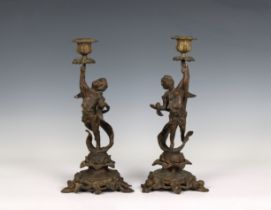 A pair of bronze figural candlesticks depicting winged putti holding aloft sconces, raised on