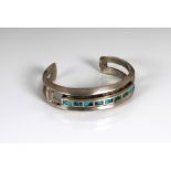 A heavy white metal bangle set with turquoise stones.