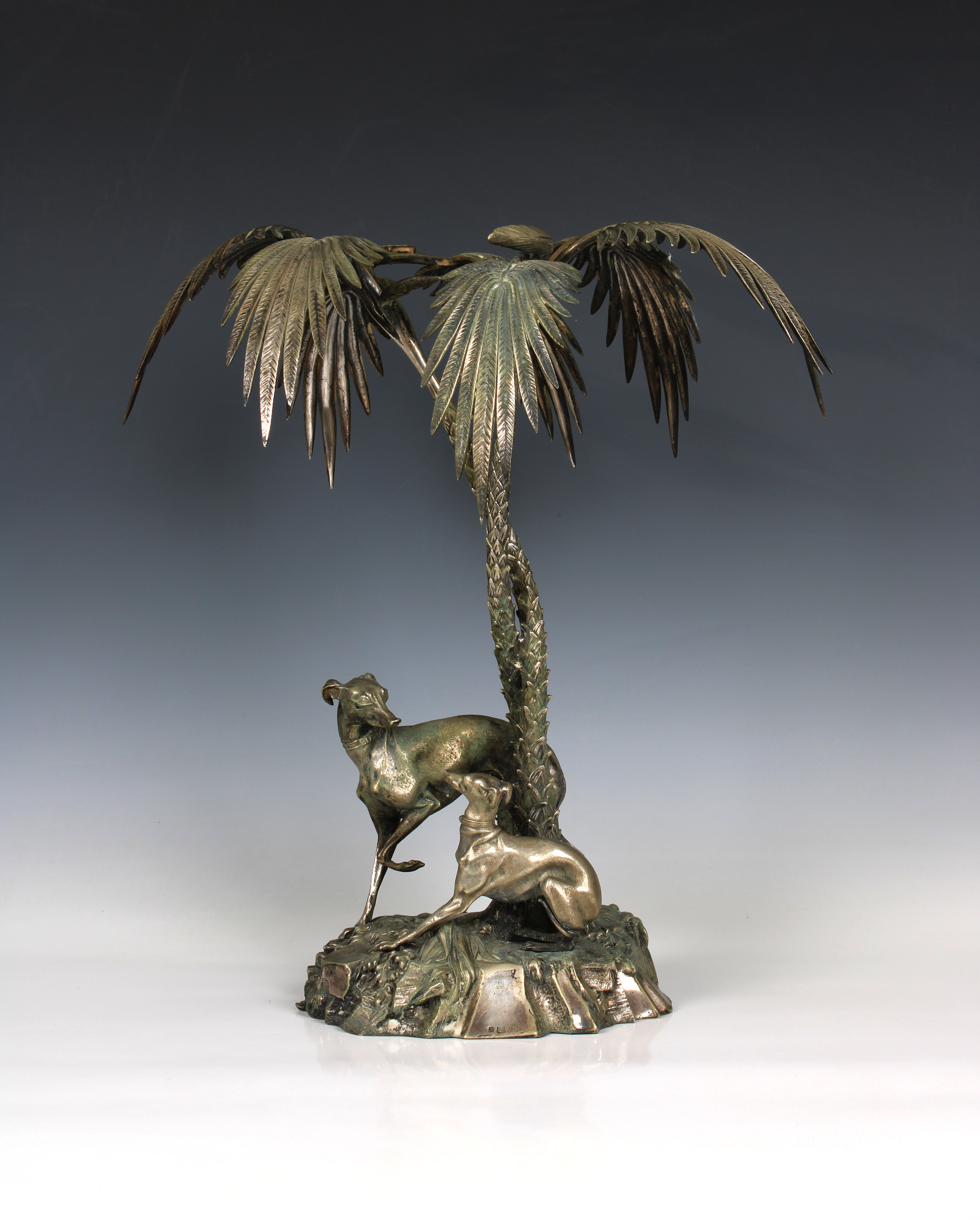 A silver plated centrepiece in the form of two greyhounds sheltering beneath palm trees