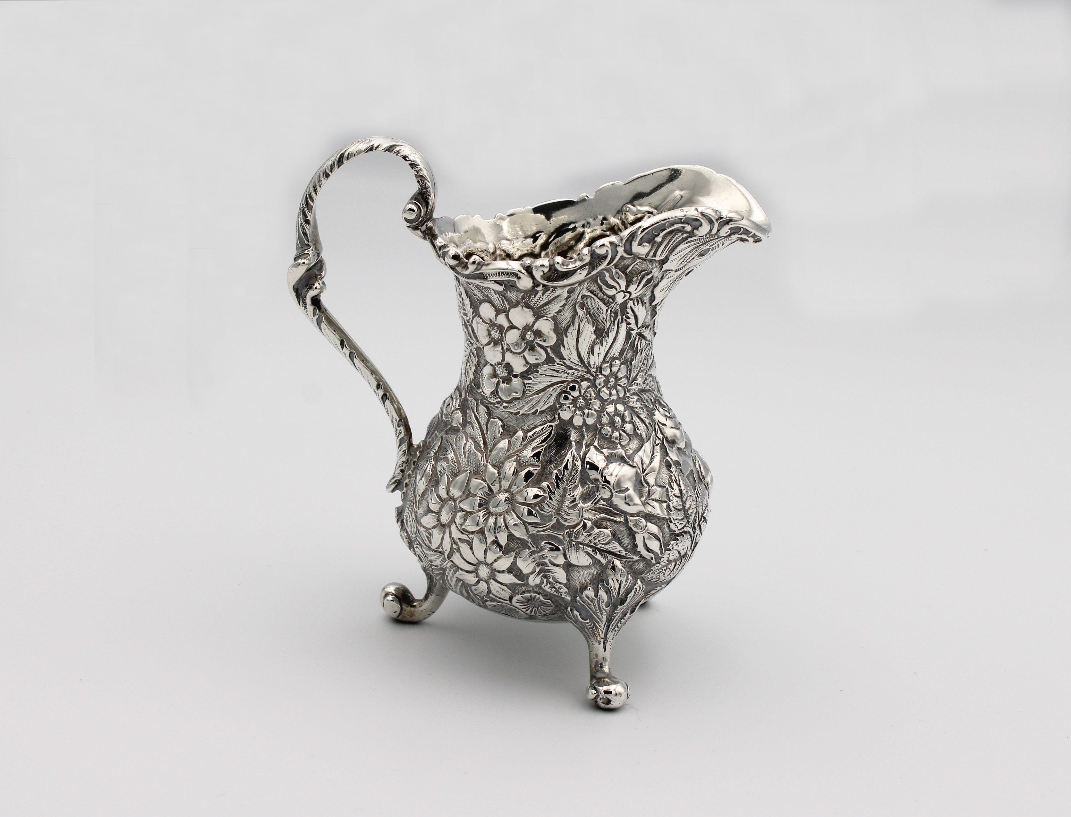 A silver milk jug heavily chased with flora