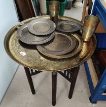 A Middle Eastern circular folding table with etched decoration, similar brass including dishes, mugs