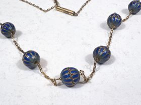 A yellow metal chain necklace with integral 7 blue enamelled beads, length 78cm.