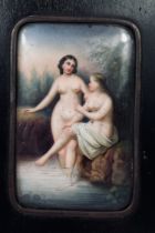 A classical hand painted ceramic panel of two nude females bathing, in ebonised frame