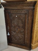 A 19th century oak corner cupboard with straight front, single door, extensive carved decoration