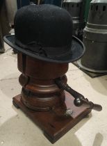 An antique wooden hat stretcher on stand with metal turning handle, and a black bowler hat