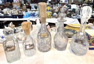 Four various cut glass decanters and a set of 5 silver plated bottle labels