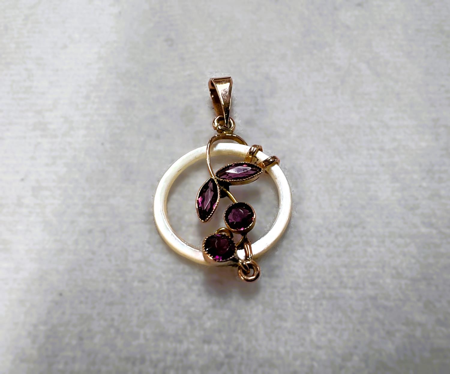 A delicate pendant formed from an open mother of pearl circlet with amethyst flower and drop in