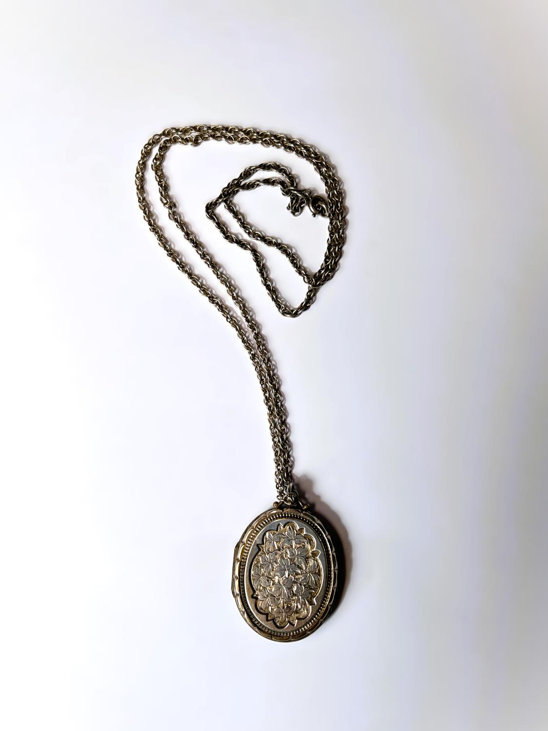 An oval chased white metal locket on later 'Prince of Wales' silver chain, length of chain 74cm