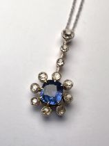 A white metal pendant in the form of a flowerhead drop with central oval sapphire surrounded by 8