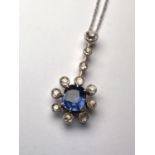 A white metal pendant in the form of a flowerhead drop with central oval sapphire surrounded by 8