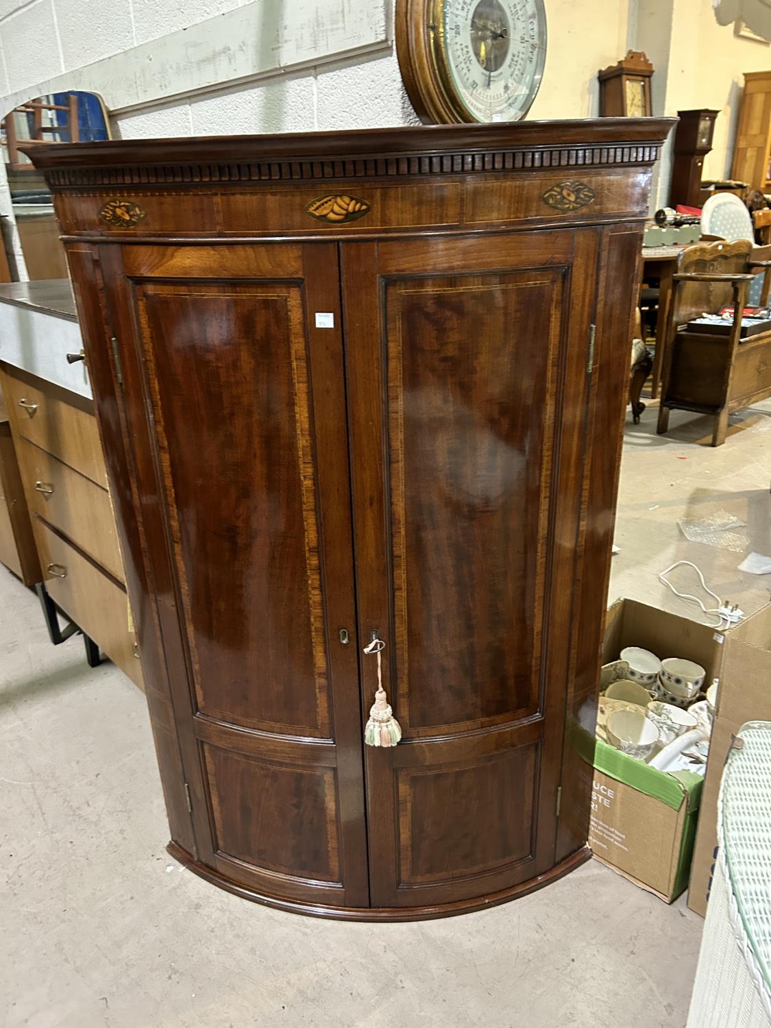 A George III mahogany corner cupboard with bow front and Sheraton style inlay, enclosed by