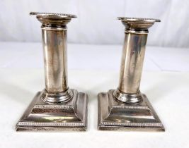 A pair of hallmarked silver dwarf candlesticks with beaded borders on square weighted bases, ht.