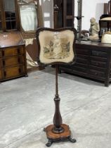 An early Victorian rosewood polescreen with needlework banner, on faceted baluster column and