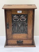 An Art -Nouveau oak smoker"s cabinet enclosed by a door with copper repousse panel of stylised