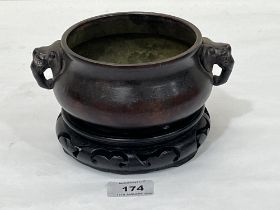 A Chinese bronze censer with elephant handles on carved wood stand. 7" diam over handles.