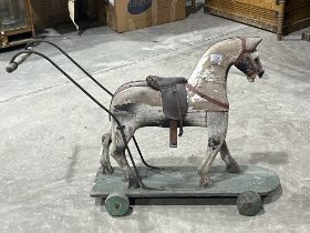 A Victorian carved pine push-along horse toy. Base 27" long. Two wheels lacking, distressed.