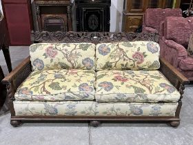 A 1930s oak carved bergere three piece sofa suite comprising a sofa (break to back) and a pair of