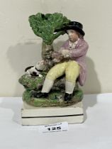 An early 19th Century Staffordshire pearlware figure of a man seated on a tree stump feeding a