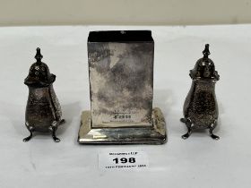 A silver matchbox stand, base weighted, and a pair of silver pepperettes.