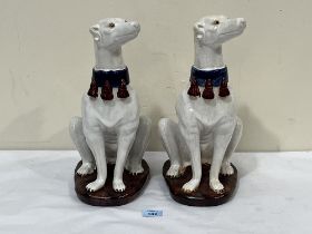 A pair of Continental glazed pottery models of seated greyhounds, each with a blue tasselled collar,