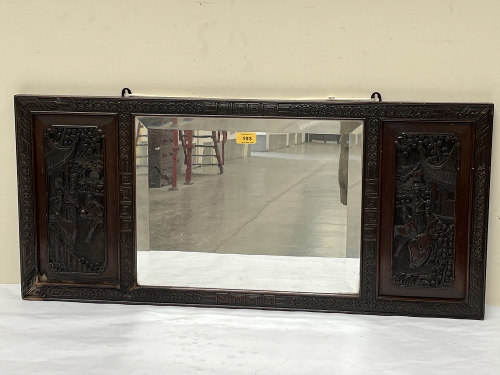 An Oriental wall mirror, the bevelled plate flanked by panels carved in bas-relief. 16½" x 36".