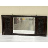 An Oriental wall mirror, the bevelled plate flanked by panels carved in bas-relief. 16½" x 36".