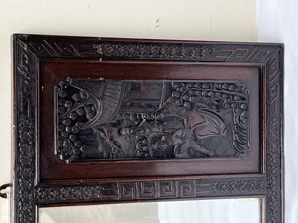 An Oriental wall mirror, the bevelled plate flanked by panels carved in bas-relief. 16½" x 36". - Image 2 of 2