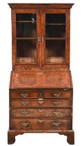 A walnut bureau-cabinet, with ogee moulded cornice and glazed doors above candle slides, the flap in