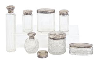 Seven Edwardian and George V silver capped cut or faceted glass bottles and jars and another