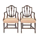 A pair of George III mahogany elbow chairs, the shield shaped back carved with husks and flowers, on