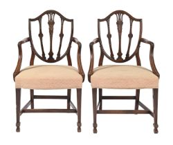 A pair of George III mahogany elbow chairs, the shield shaped back carved with husks and flowers, on