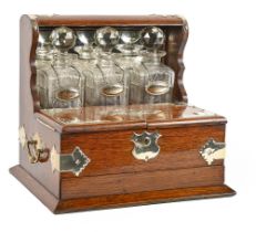 An EPNS mounted oak tantalus, early 20th c, with set of three cut glass decanters, stoppers and