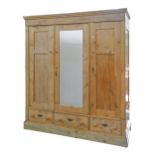 An early 20th c waxed and panelled pine triple wardrobe,  the central section with mirrored door,