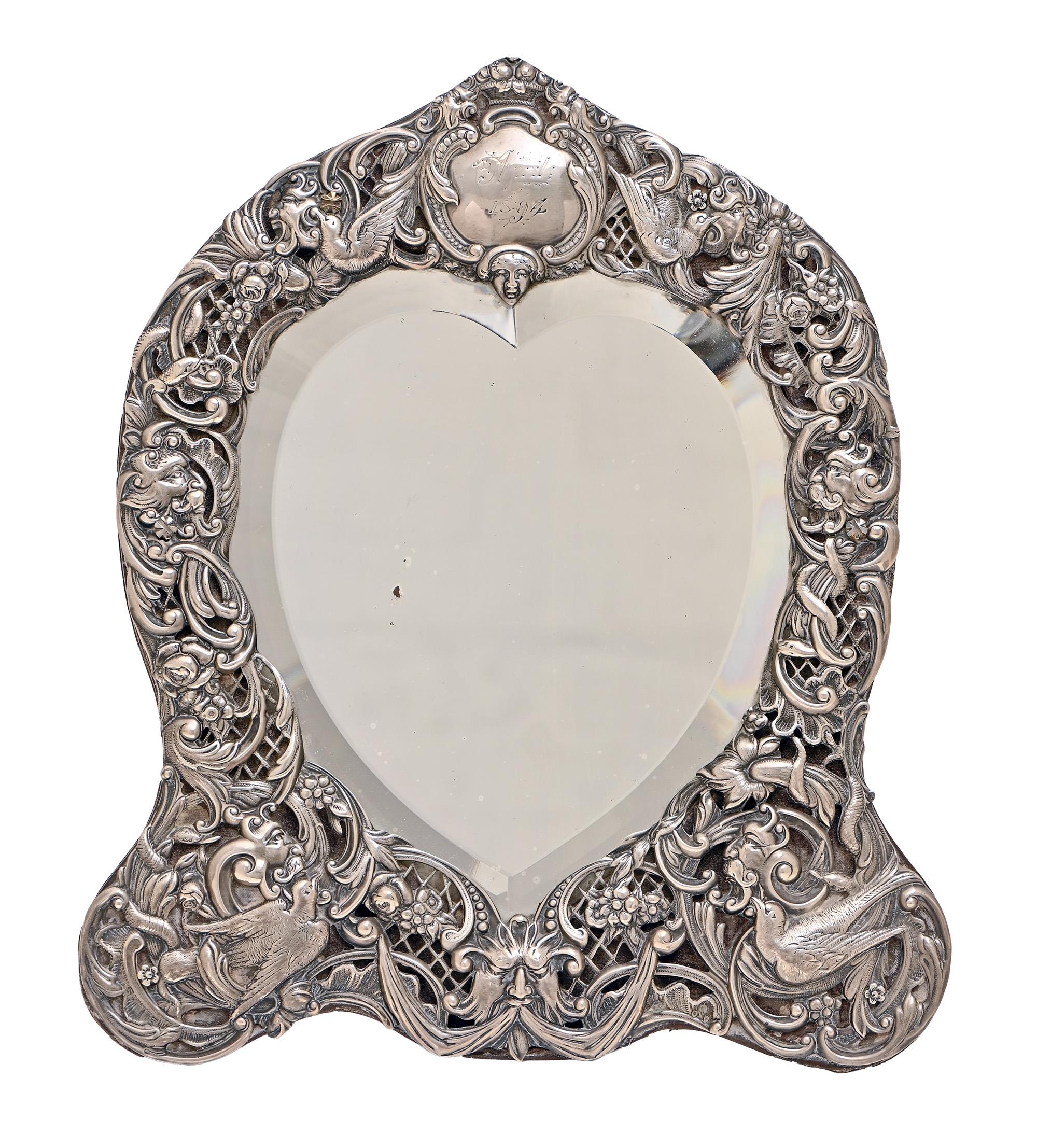 A Victorian heart shaped silver dressing mirror, the die stamped trellis mount decorated with
