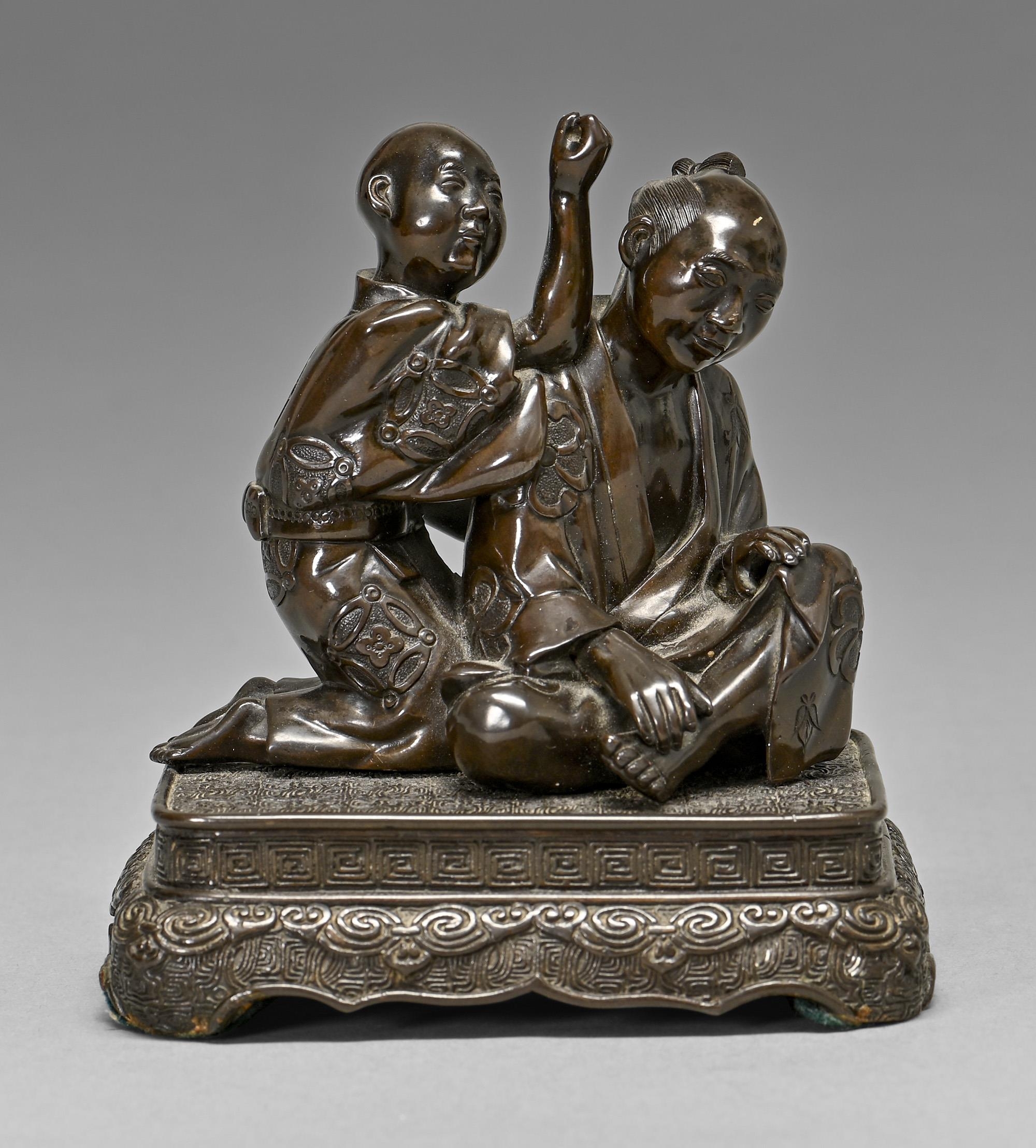 A Japanese bronze group, Meiji period, of a seated man and boy kneeling at his shoulder, mounted