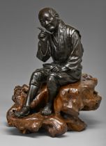 A Japanese bronze sculpture of a man, seated with contemplative expression holding his tobacco
