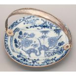 A Chinese blue and white plate, 18th c, painted with a flowering plant, bamboo and fence on a scroll