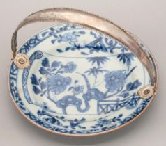 A Chinese blue and white plate, 18th c, painted with a flowering plant, bamboo and fence on a scroll