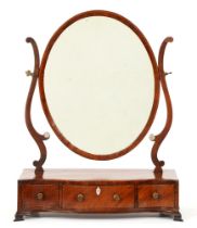 A George III mahogany dressing mirror, the frame to the oval plate and serpentine base with barber
