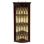 An Edwardian serpentine mahogany hanging corner cabinet, the glazed door with lancet and diamond